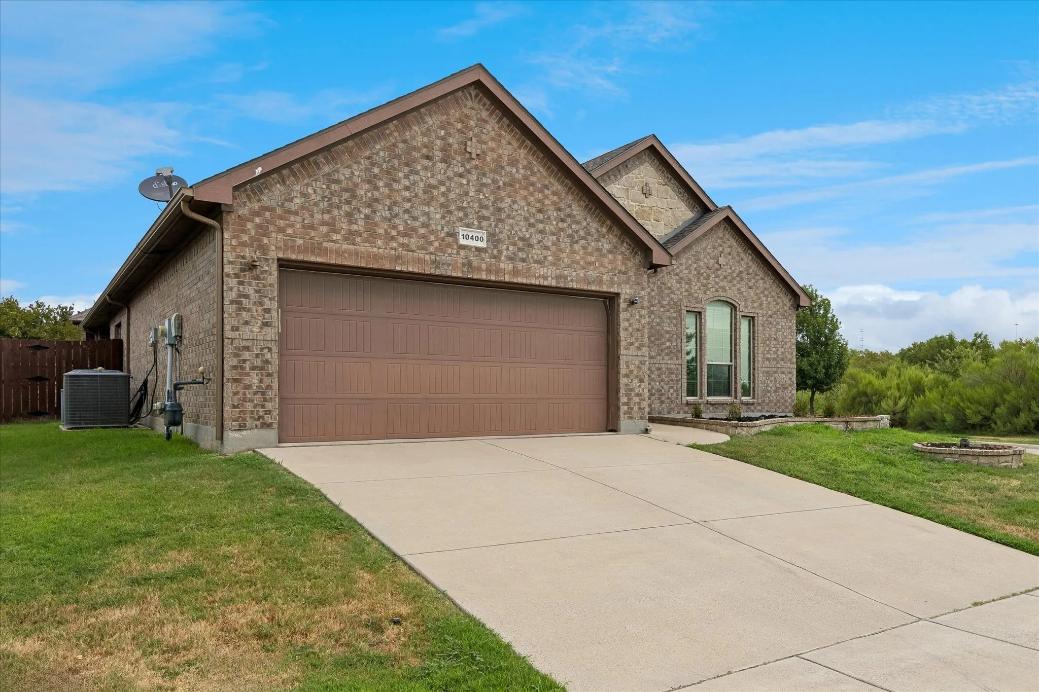 Brick exterior with a peaked roofline, attached two-car garage, concrete driveway, and a prominent arched window