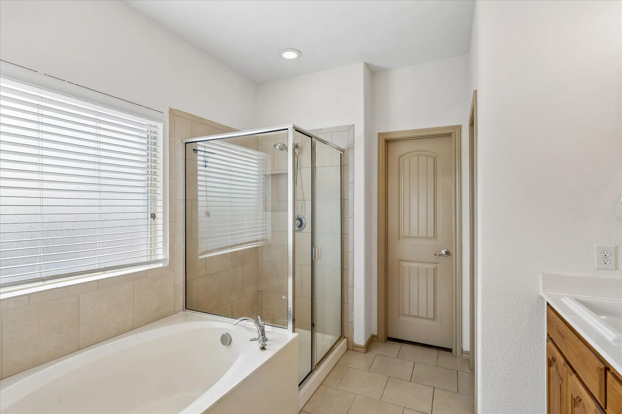 Built-in bathtub, glass-enclosed shower, tiled flooring, recessed lighting, and a wood vanity with a white countertop