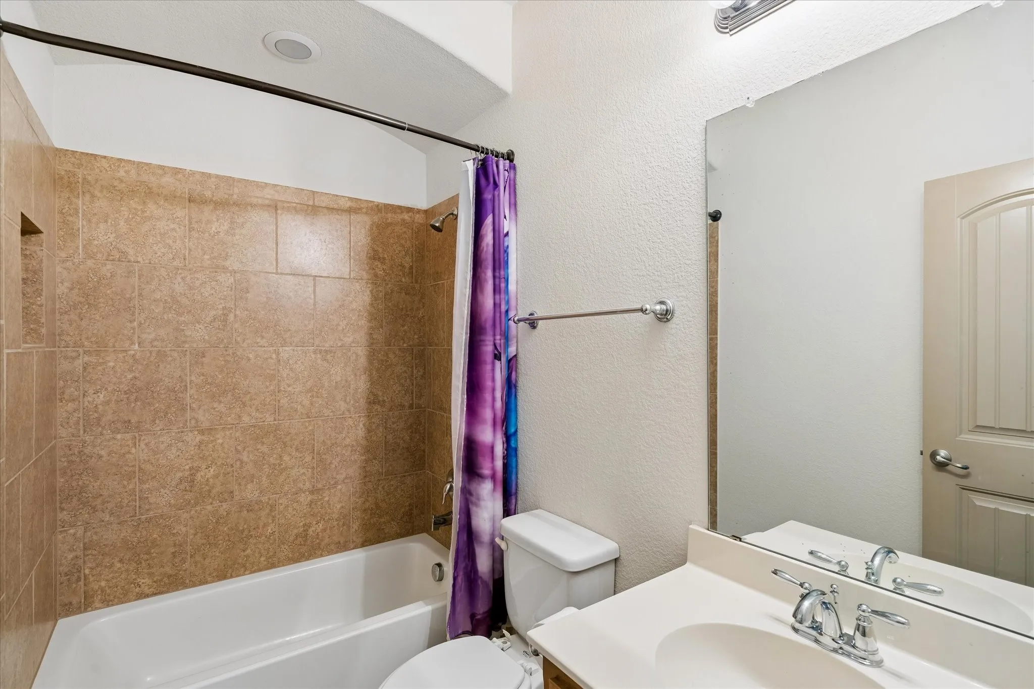Bathtub with integrated shower, tiled surround, and built-in niche