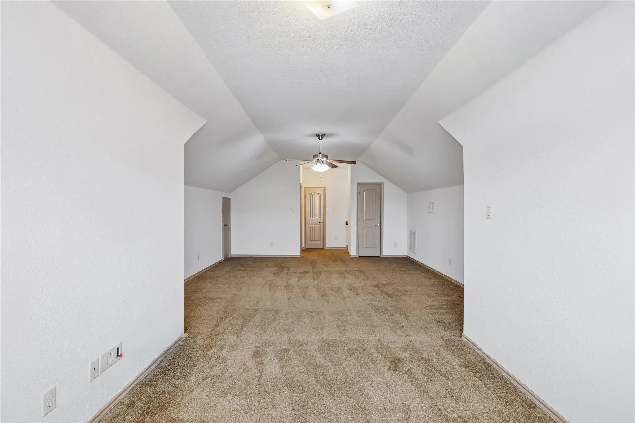 Expansive room with vaulted ceilings, neutral carpet flooring, and a ceiling fan