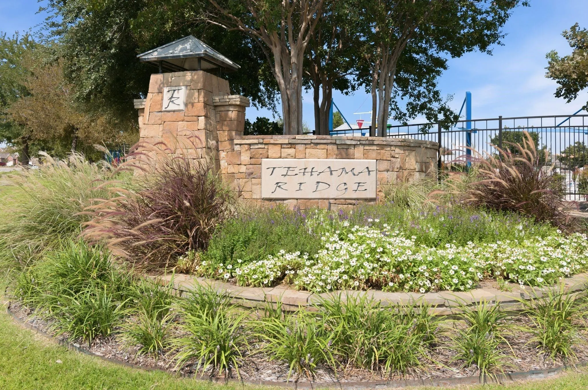 Stone-clad entry monument featuring a decorative cap, integrated signage, and diverse low-maintenance landscaping