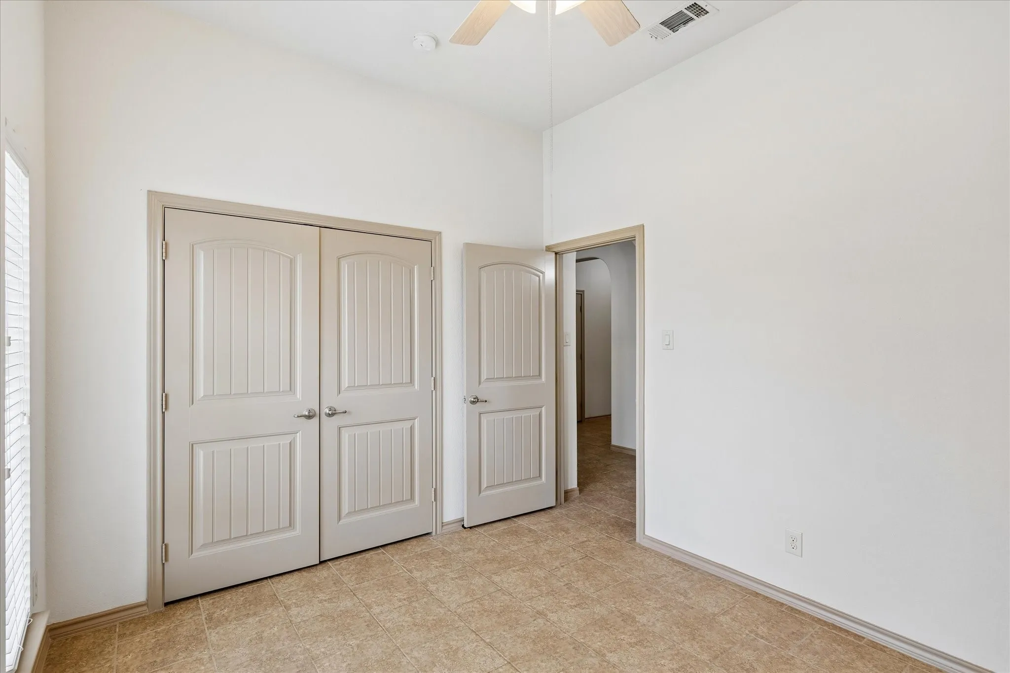 Vaulted ceiling with a ceiling fan, light-toned tile flooring, and solid panel doors