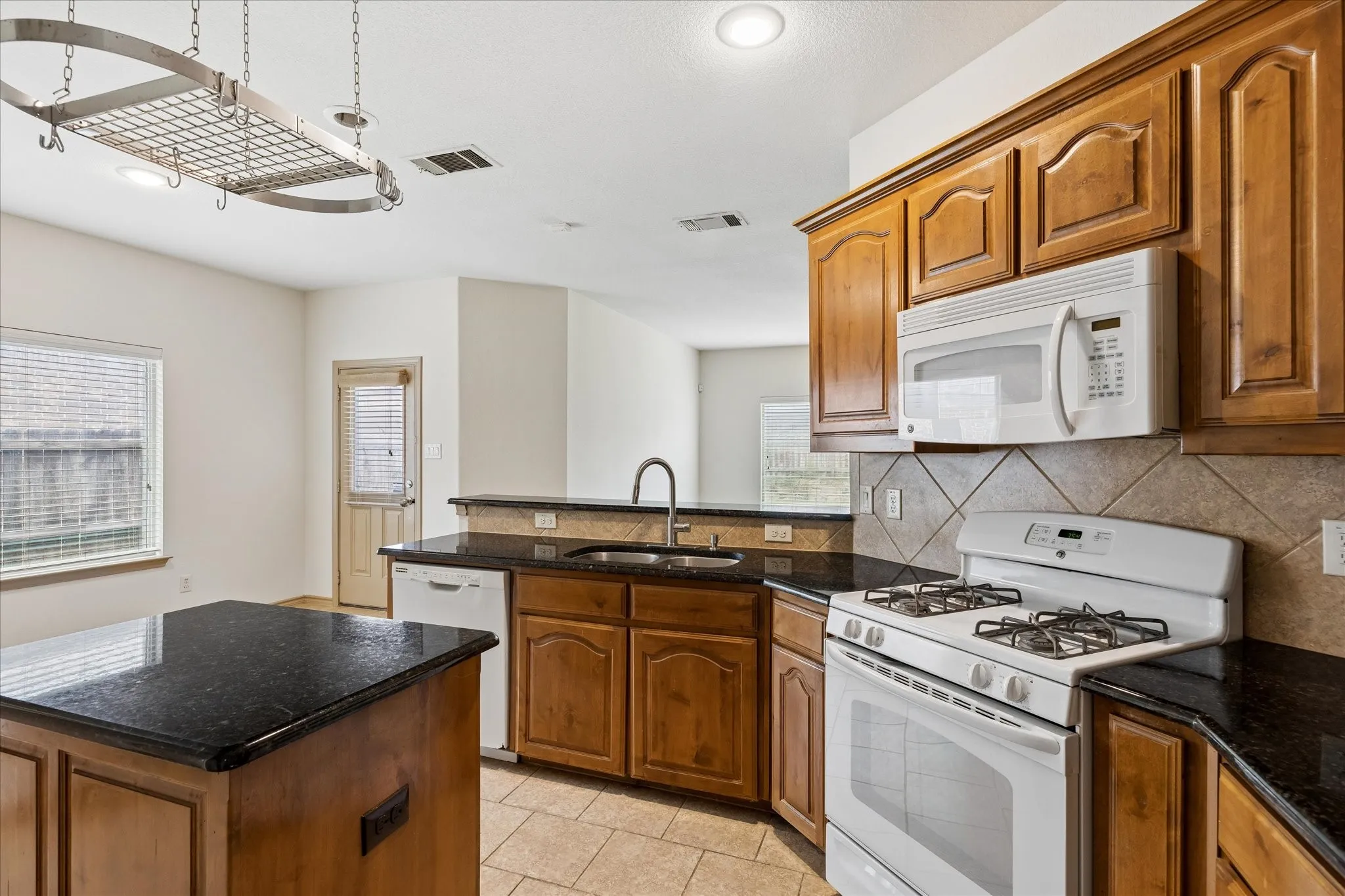Kitchen featuring wood cabinetry, dark countertops, a built-in microwave, a gas range, and tile flooring