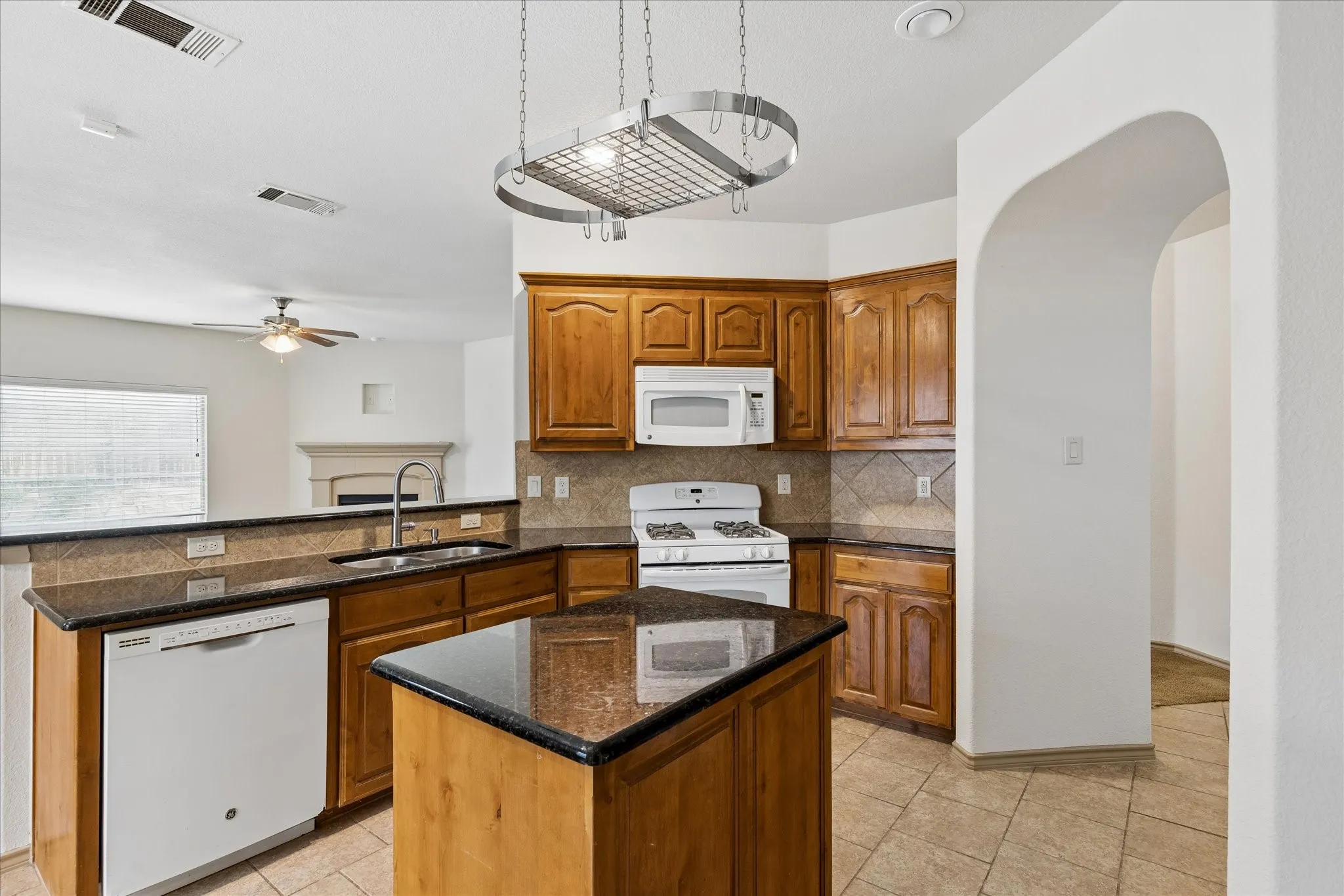 Kitchen featuring wood cabinetry, dark countertops, a central island, a built-in oven, and a dishwasher