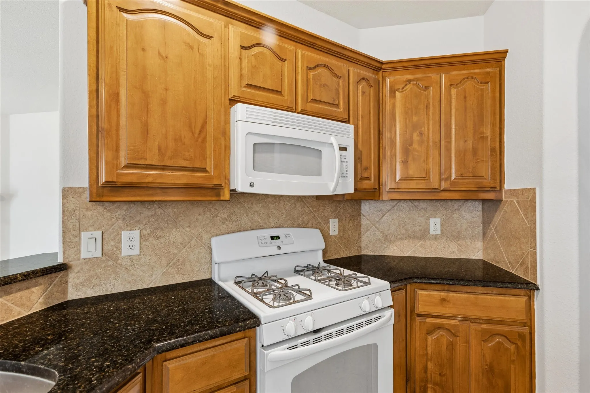 Wood-finish cabinetry with crown molding, dark speckled countertops, and a tiled backsplash