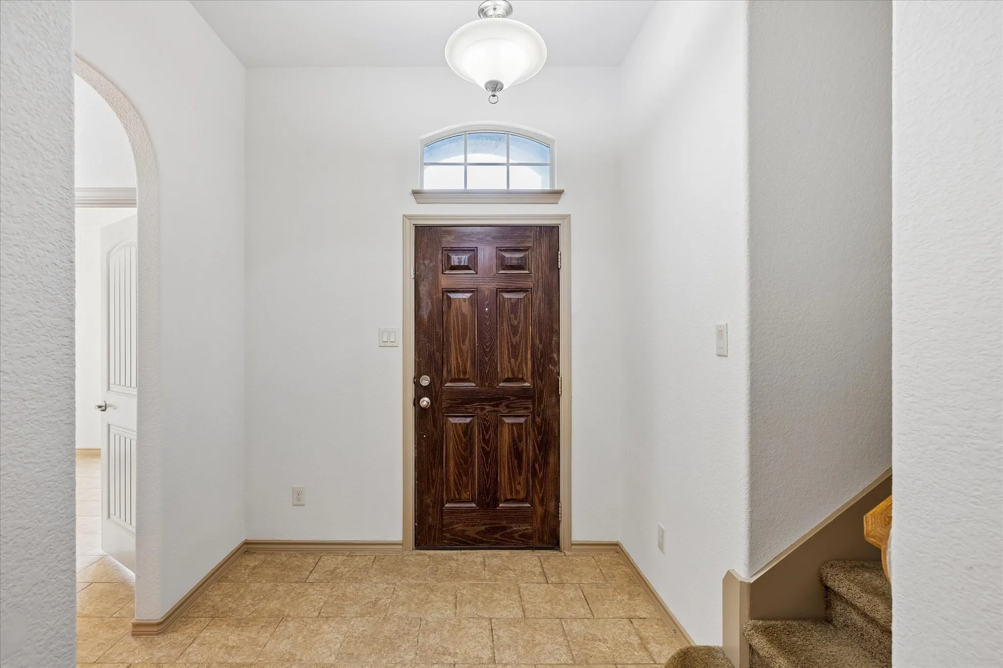 Entryway featuring a paneled wood door, arched transom window, overhead flush mount light fixture, and tile flooring