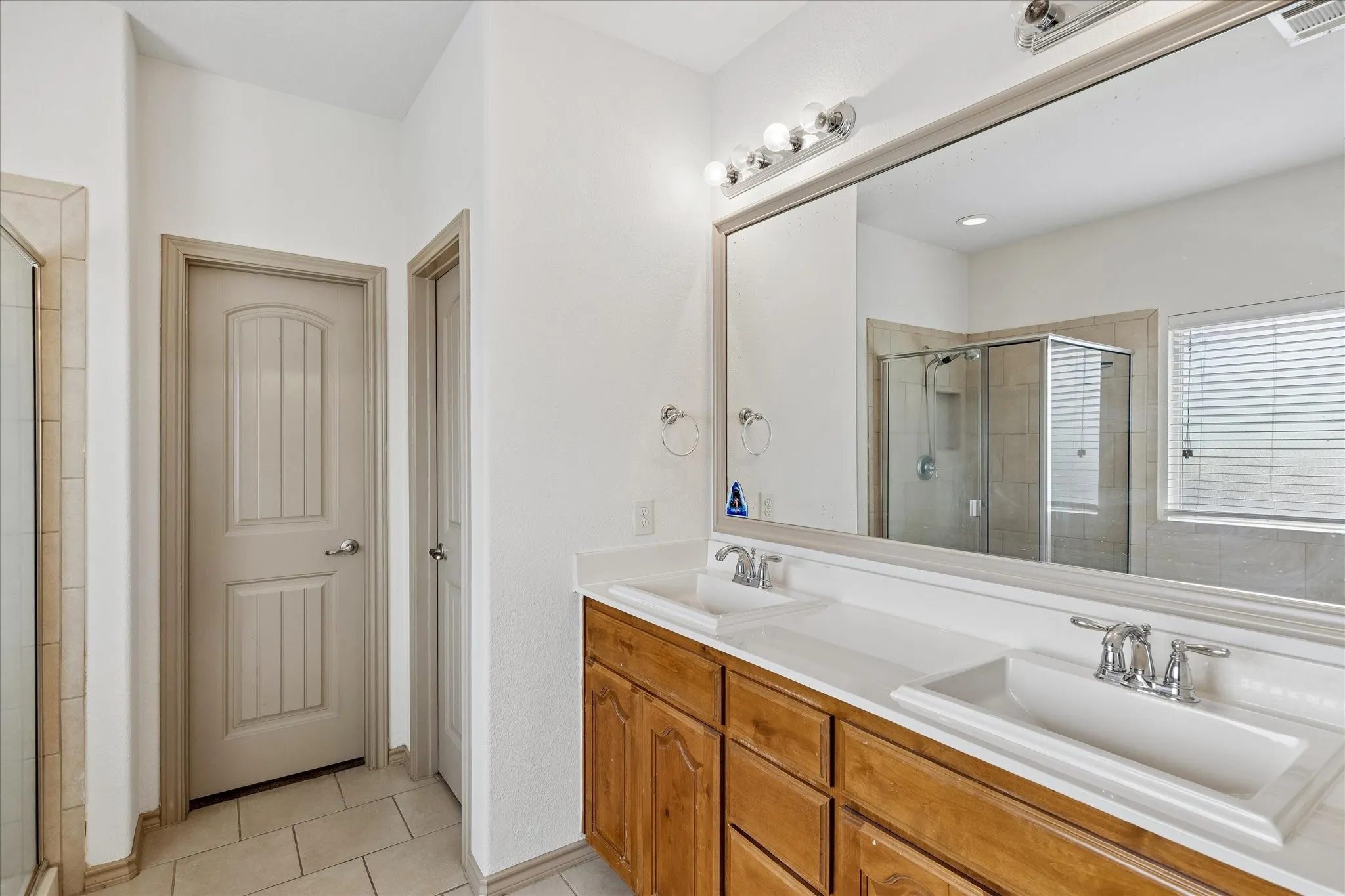 Dual vanity with integrated sinks and chrome fixtures, framed mirror, and wood-finish cabinetry