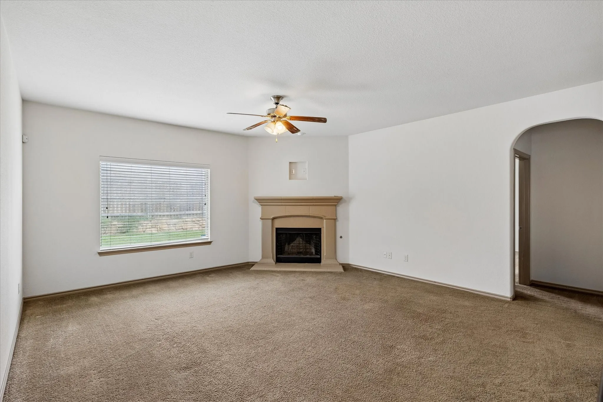 Spacious living area with neutral carpet flooring, ceiling fan with integrated lighting, and a corner fireplace with a wood-finish mantel