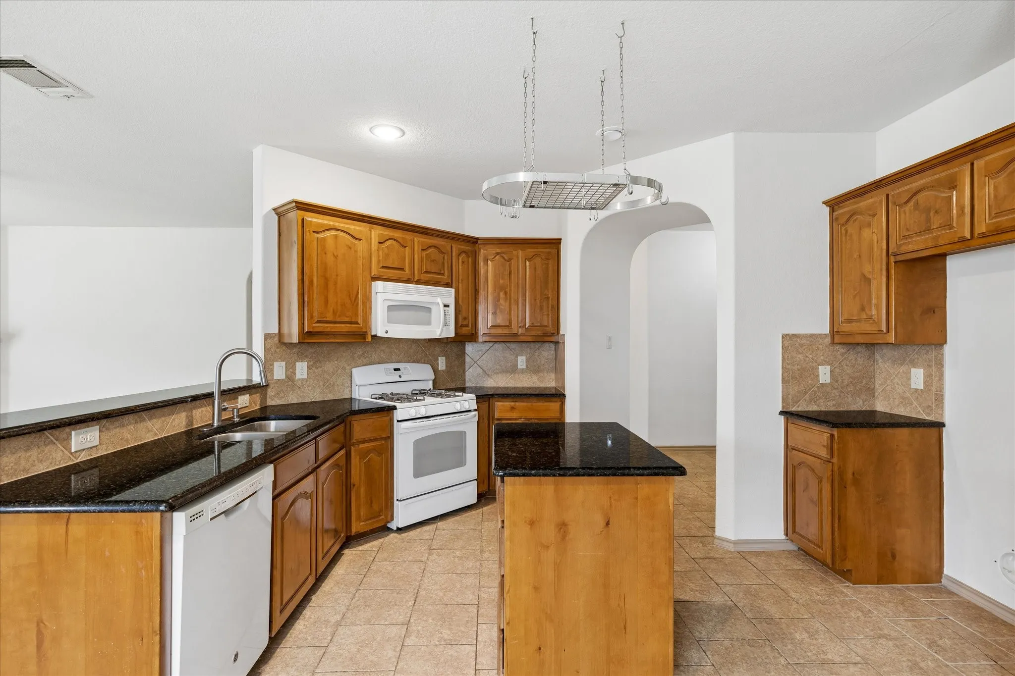 Kitchen featuring wood-finish cabinetry, black countertops, tile backsplash, and a central island