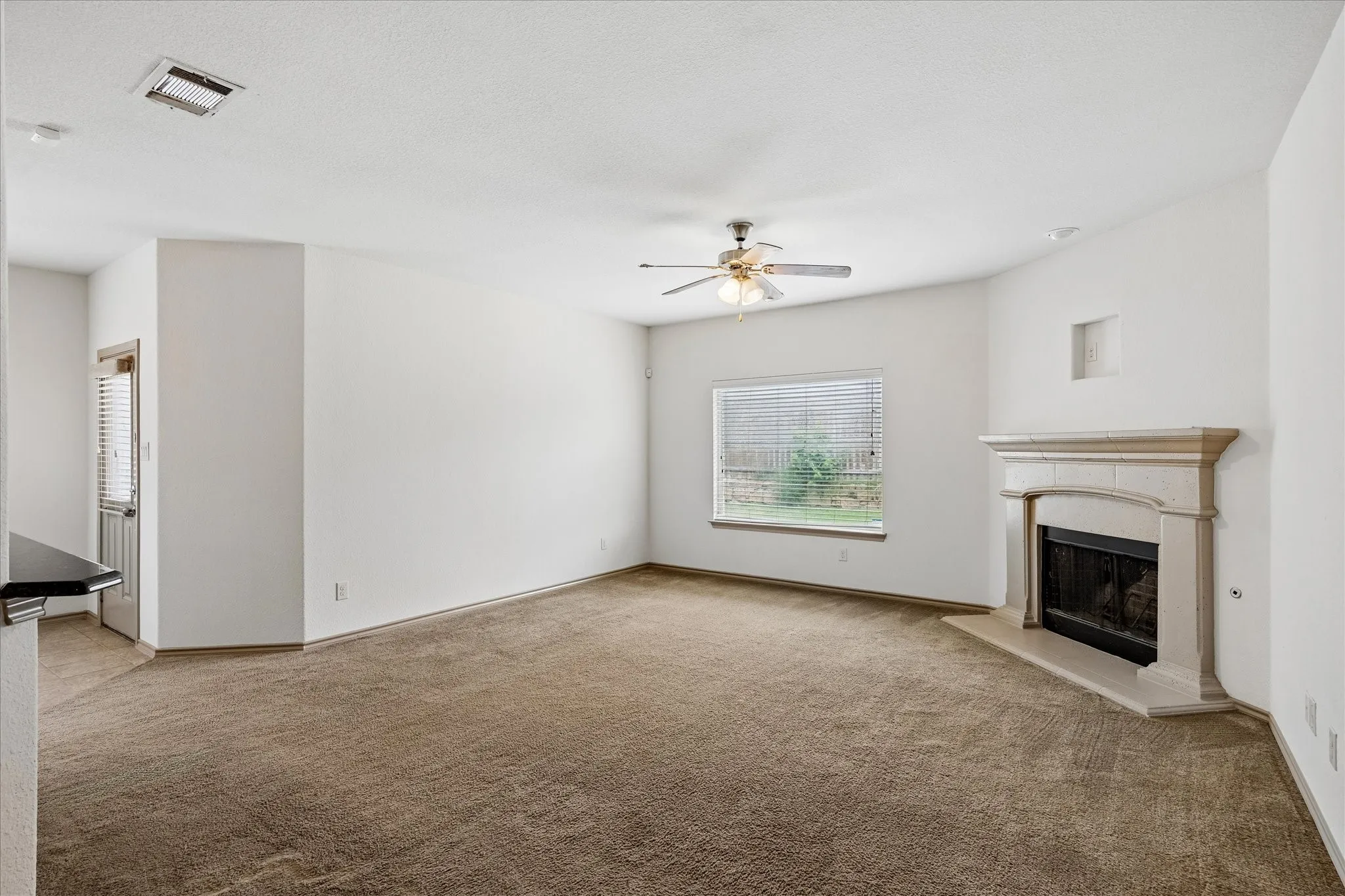 Spacious interior with neutral carpeting, a decorative fireplace, and a ceiling fan