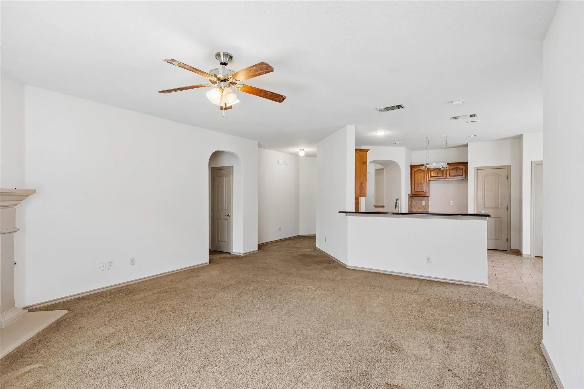 Expansive room featuring a ceiling fan with integrated lighting, a fireplace mantel, and an arched doorway