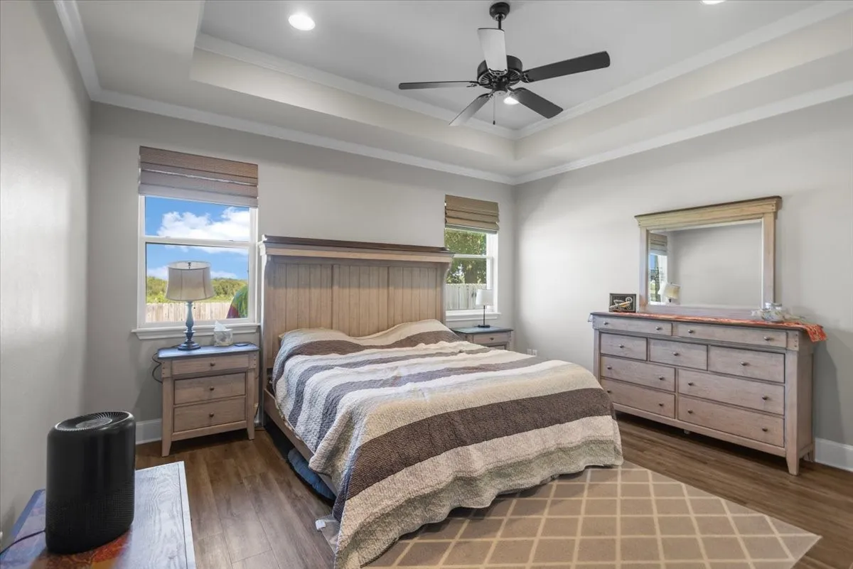 Primary suite with tray ceiling, crown molding, and dual windows flanking the bed wall.