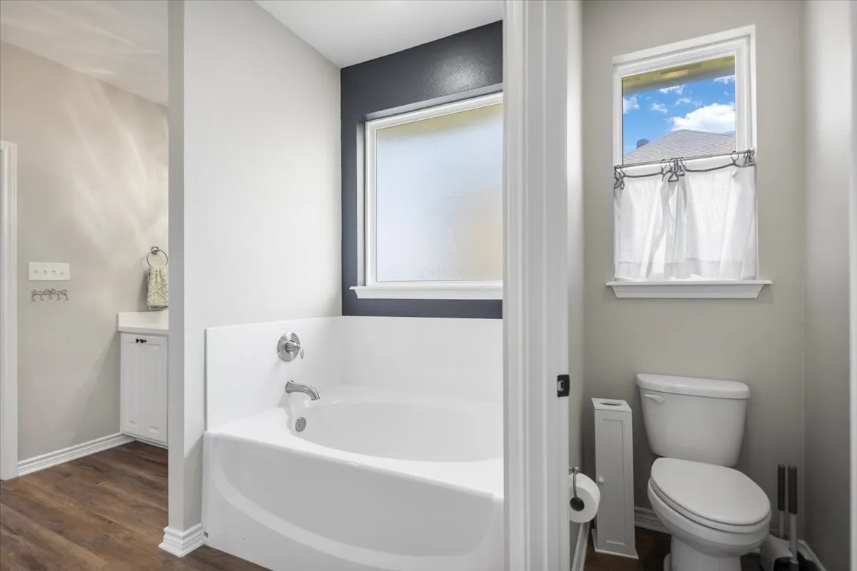 Soaking tub set in a windowed alcove with tile surround skirt and chrome fixtures.