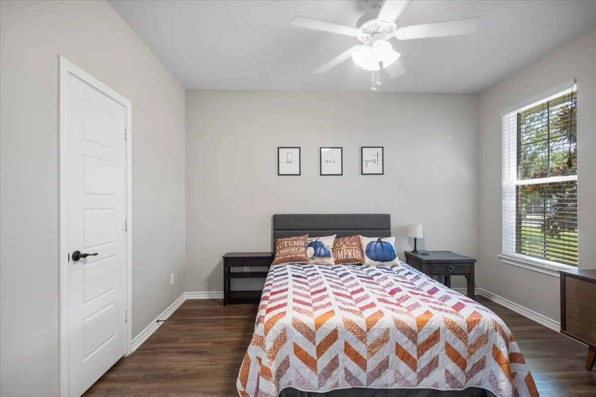 Bedroom with wood-look flooring, ceiling fan, and a window with view of mature trees.