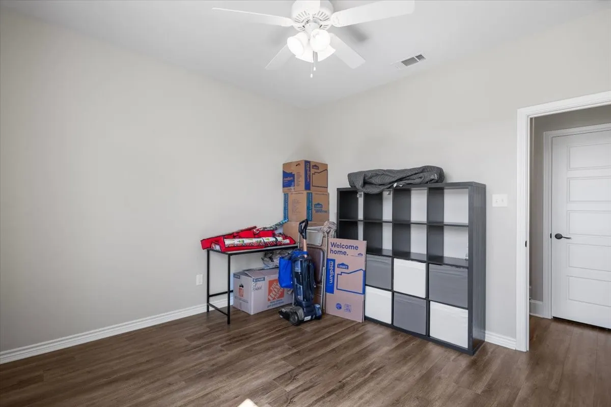  Secondary bedroom with wood-look flooring, ceiling fan, and a large window overlooking the front yard.