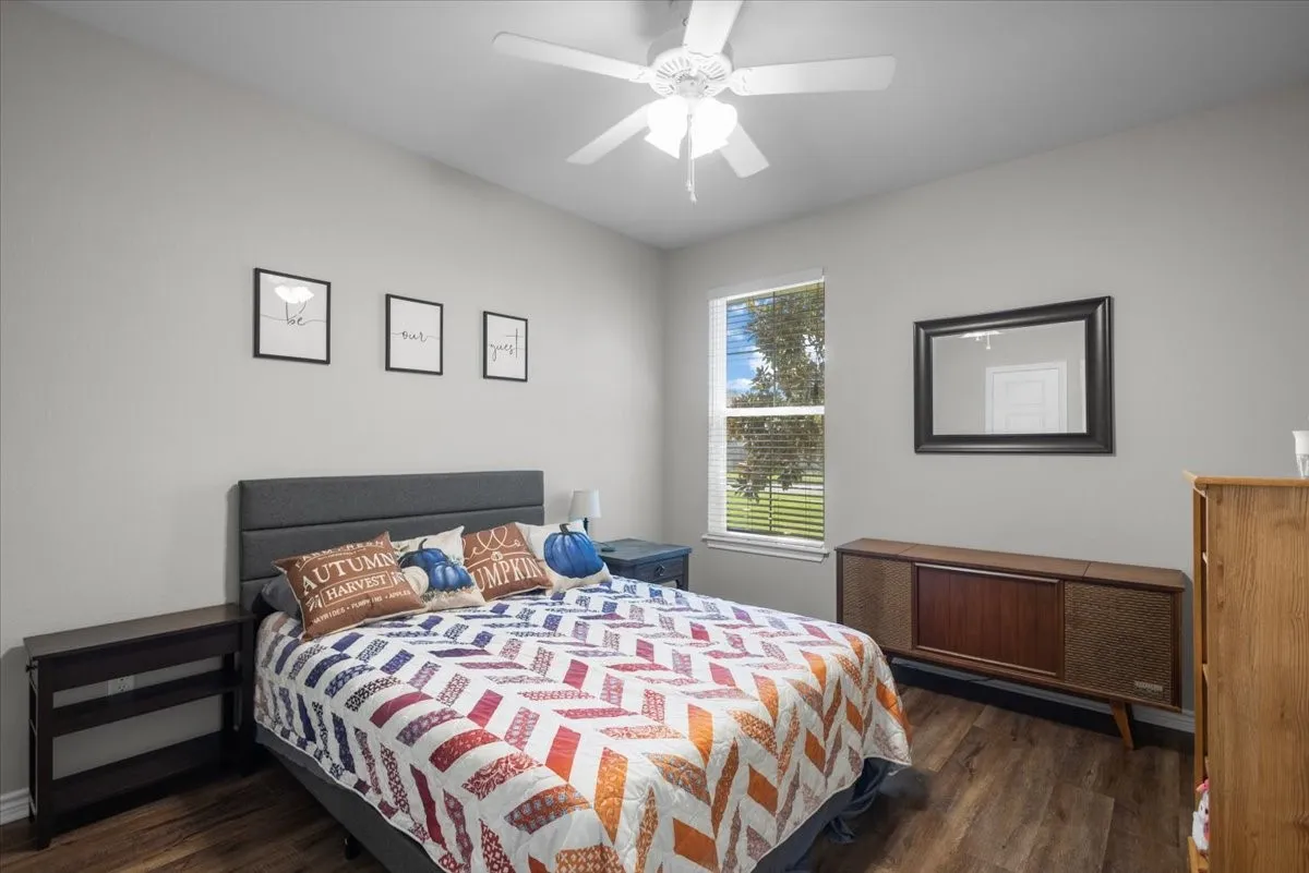 Bedroom with wood-look flooring, ceiling fan, and a window with view of mature trees.