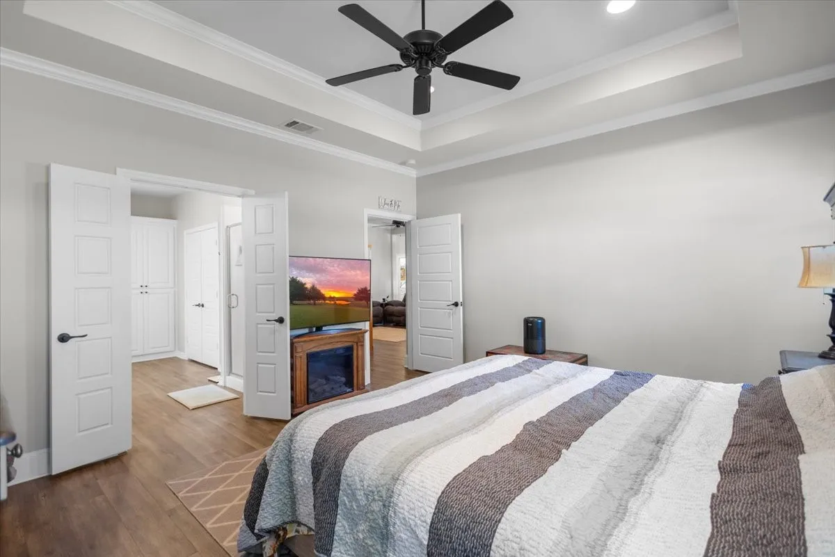 Primary suite with tray ceiling, crown molding, and dual windows flanking the bed wall.