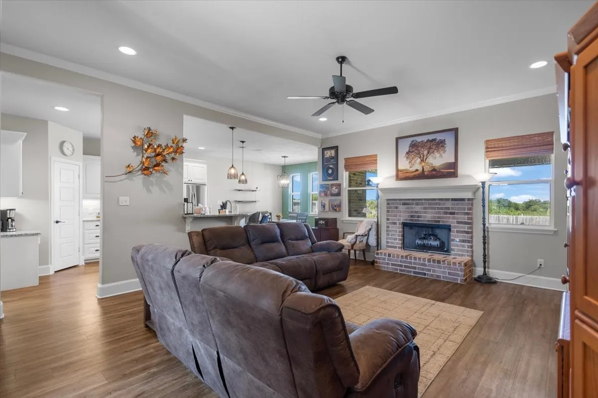 open flow into the kitchen, brick fireplace with mantel, and large windows on both sides bringing in natural light.