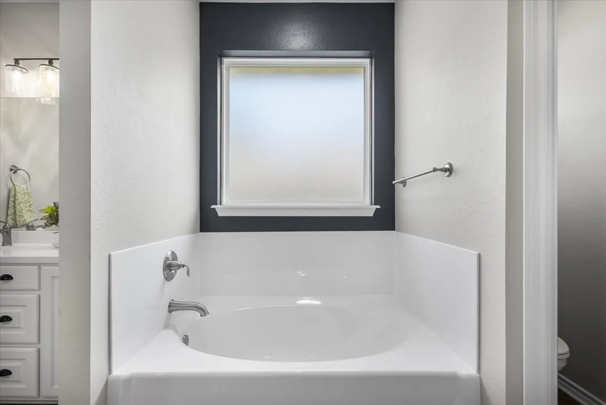 Soaking tub set in a windowed alcove with tile surround skirt and chrome fixtures.
