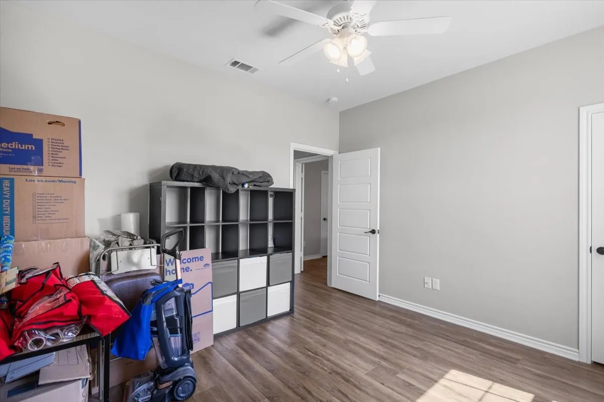  Secondary bedroom with wood-look flooring, ceiling fan, and a large window overlooking the front yard.