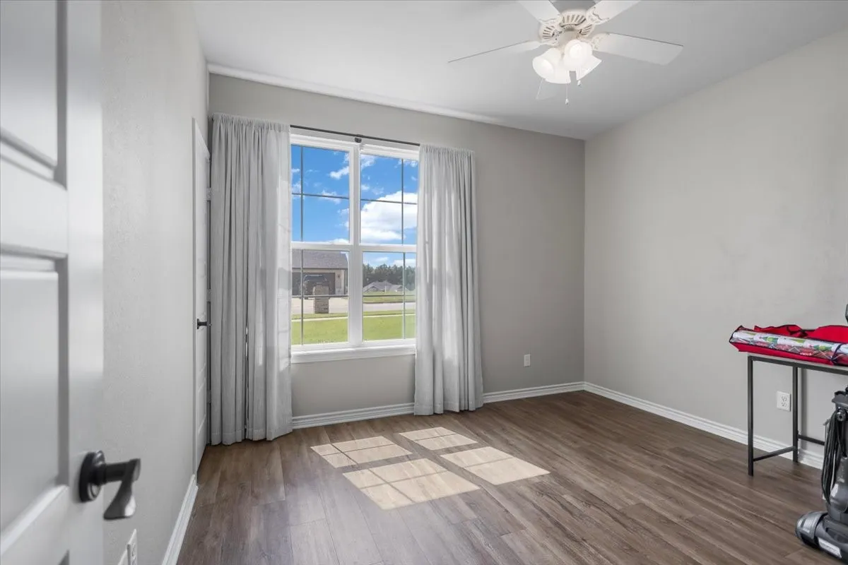 Secondary bedroom with wood-look flooring, ceiling fan, and a large window overlooking the front yard.