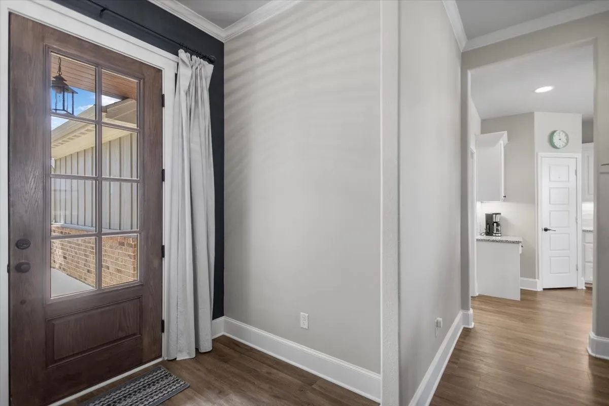 Foyer with wood-look flooring and glass-panel front door, opening to the kitchen and hallway.