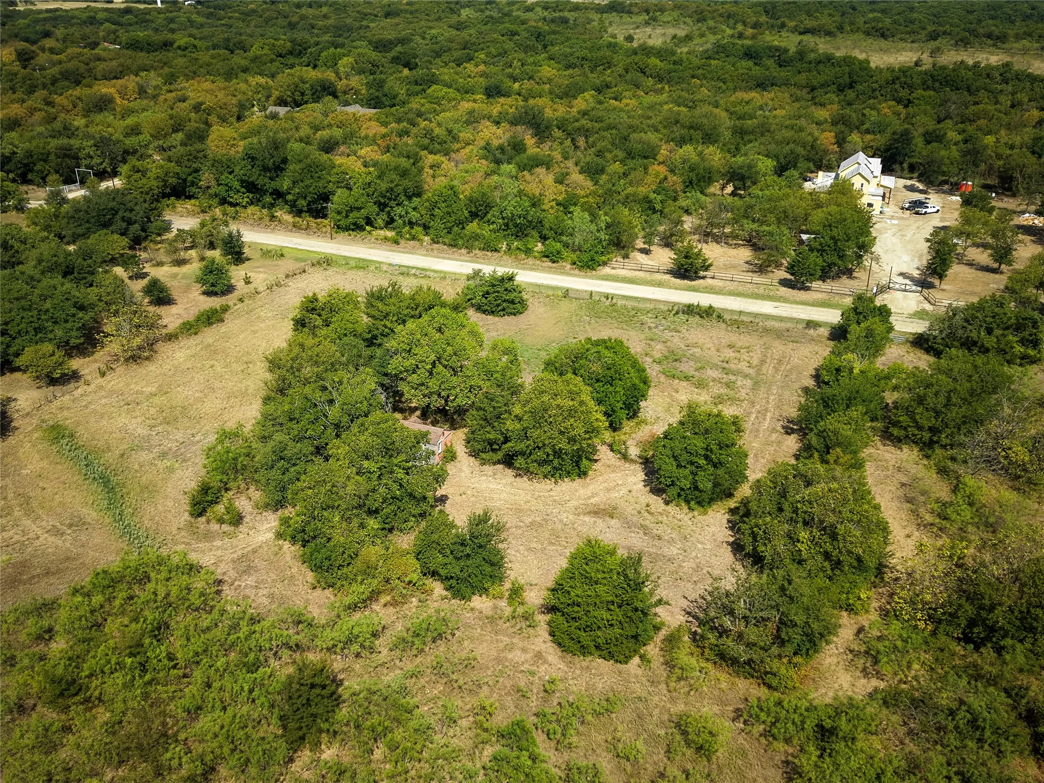 Expansive land parcel featuring mature trees, open clearings, and a gravel road