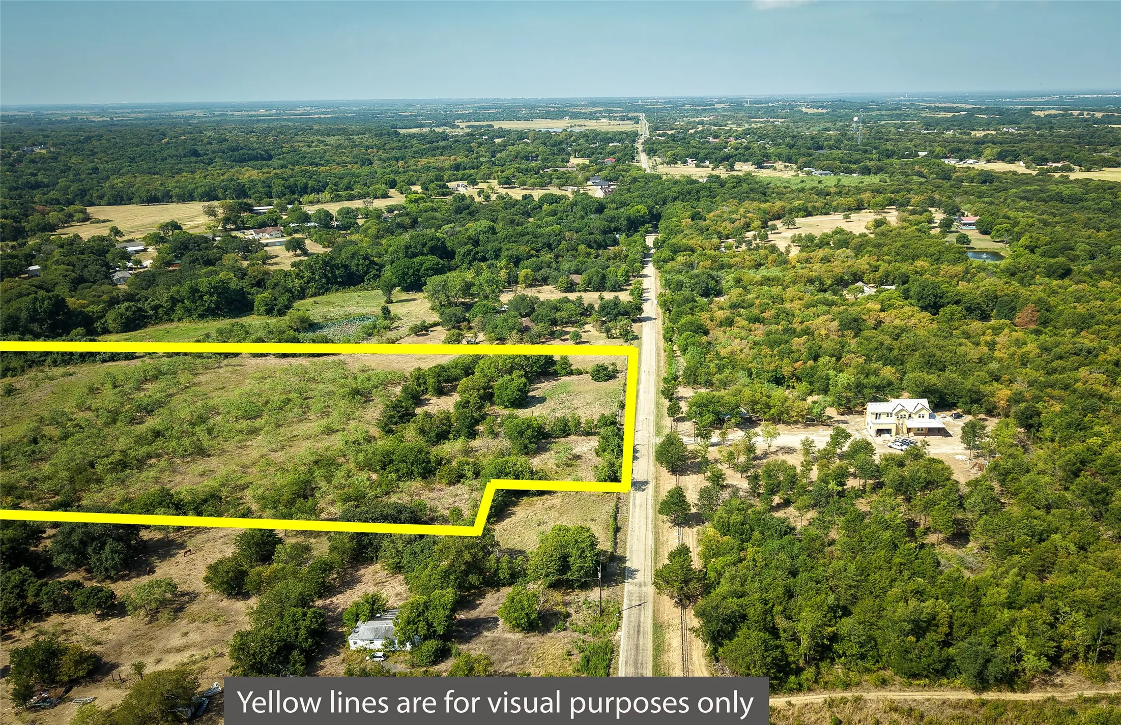 Expansive land parcel featuring a mix of open areas and mature trees, bordered by a paved road