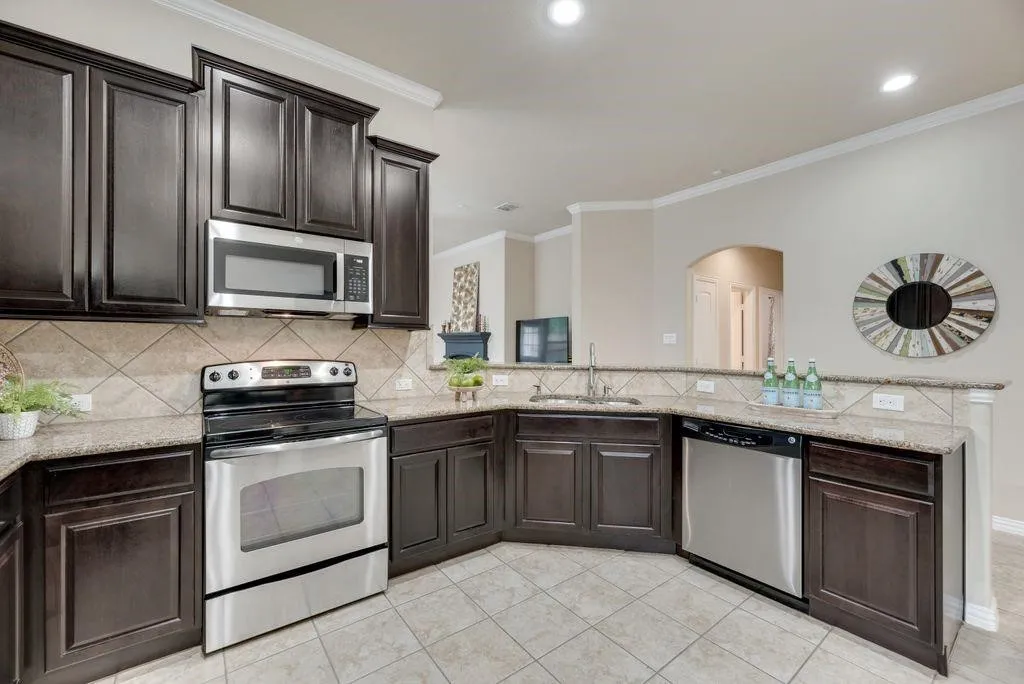 Kitchen featuring appliances with stainless steel finishes, arched walkways, backsplash, crown molding, and dark brown cabinets