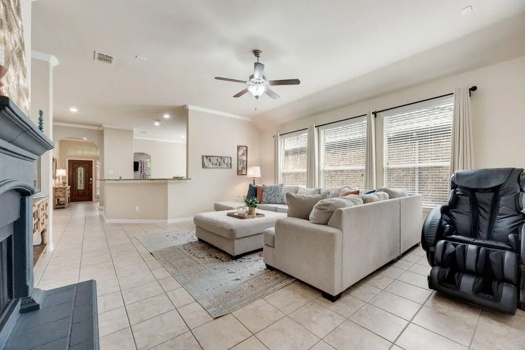 Living area featuring light tile patterned floors, arched walkways, ceiling fan, crown molding, and a fireplace