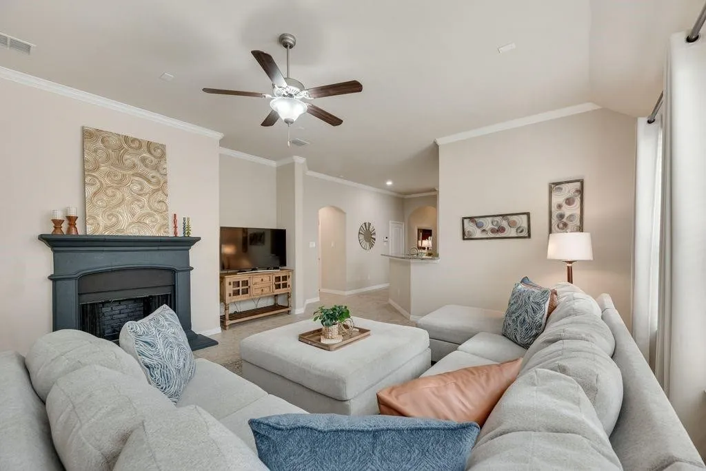 Living room with arched walkways, ceiling fan, ornamental molding, a fireplace, and light colored carpet