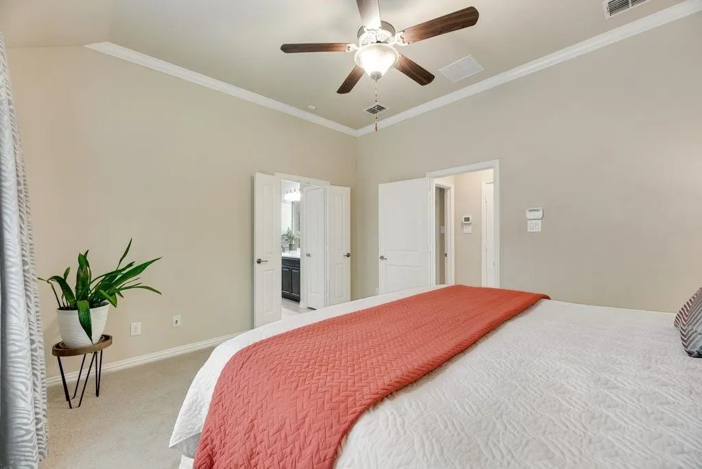 Bedroom with light carpet, crown molding, a ceiling fan, and ensuite bathroom