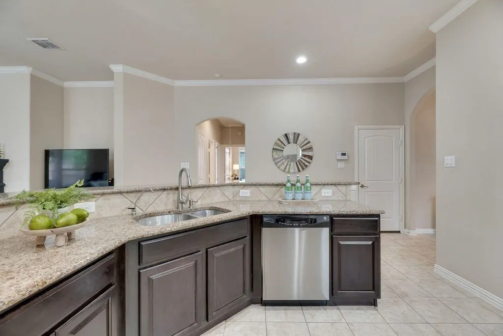Kitchen with stainless steel dishwasher, arched walkways, crown molding, and light stone counters