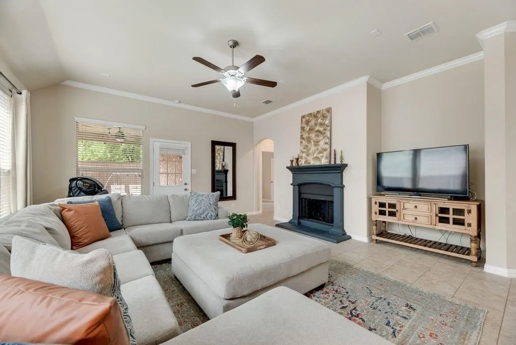 Living area featuring tile patterned floors, arched walkways, ceiling fan, ornamental molding, and a fireplace with raised hearth