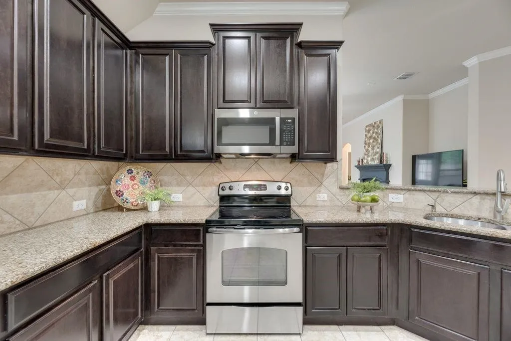Kitchen featuring appliances with stainless steel finishes, light stone countertops, dark brown cabinetry, and crown molding
