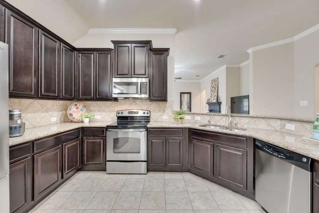 Kitchen with stainless steel appliances, backsplash, crown molding, light tile patterned flooring, and light stone countertops