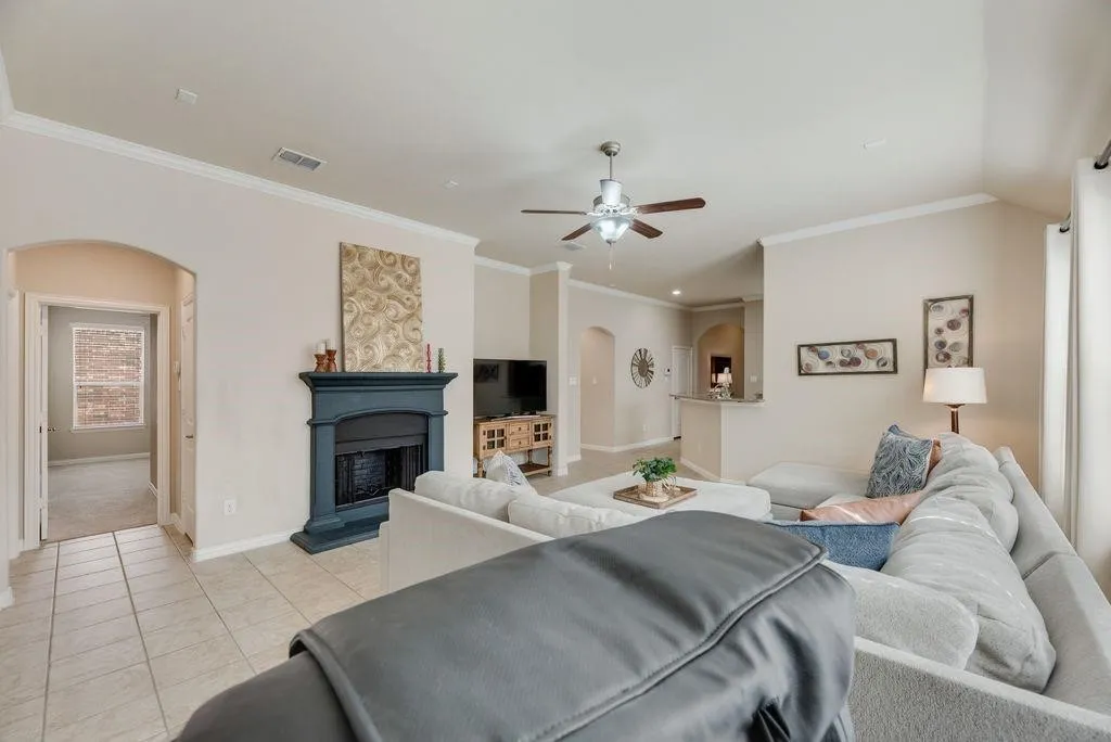 Living area featuring arched walkways, a ceiling fan, light tile patterned floors, crown molding, and a fireplace with raised hearth