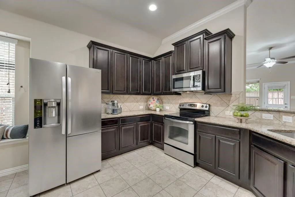 Kitchen featuring stainless steel appliances, light tile patterned floors, tasteful backsplash, light stone counters, and dark brown cabinets