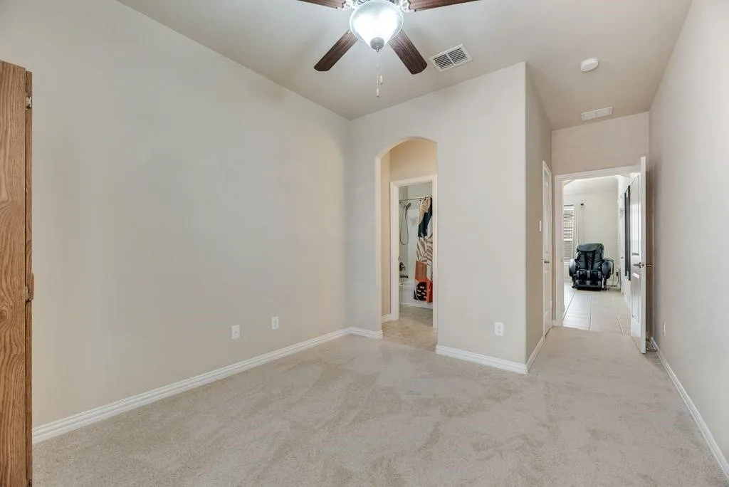 Unfurnished bedroom featuring arched walkways, light carpet, and ceiling fan