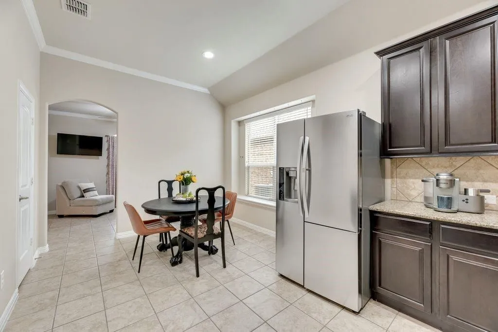 Kitchen featuring stainless steel refrigerator with ice dispenser, arched walkways, ornamental molding, dark brown cabinets, and backsplash