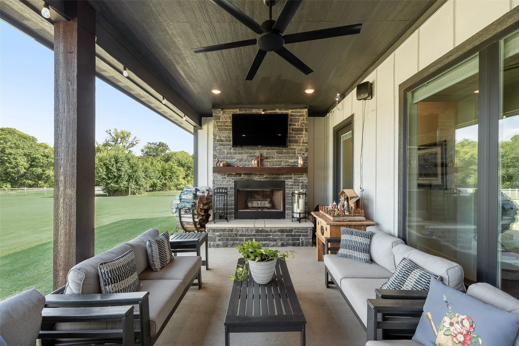 Covered patio featuring a stone fireplace with a wood mantle, a ceiling fan, recessed lighting, and a large sliding glass door
