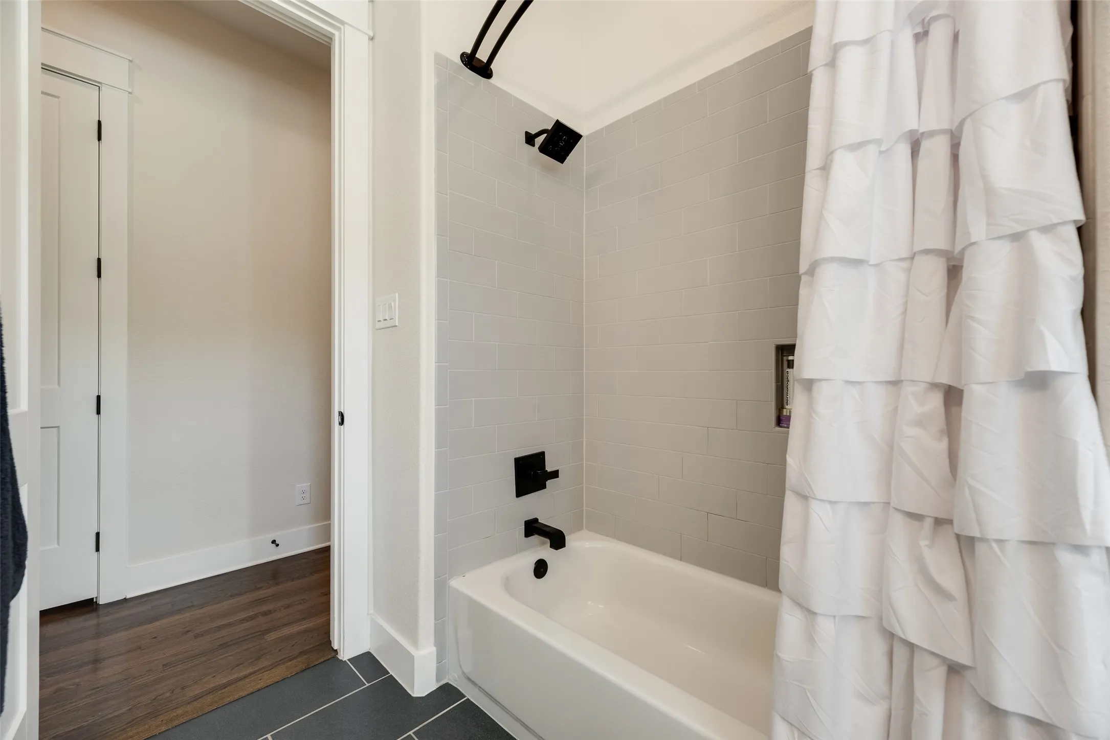 Bathroom featuring a white tub, matte black fixtures, light gray subway tile surround, and dark gray tile flooring