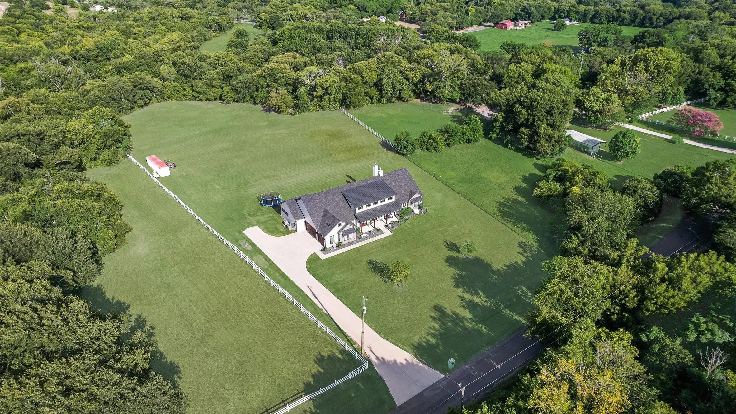 Expansive property featuring a modern residence with a dark roof and a long paved driveway