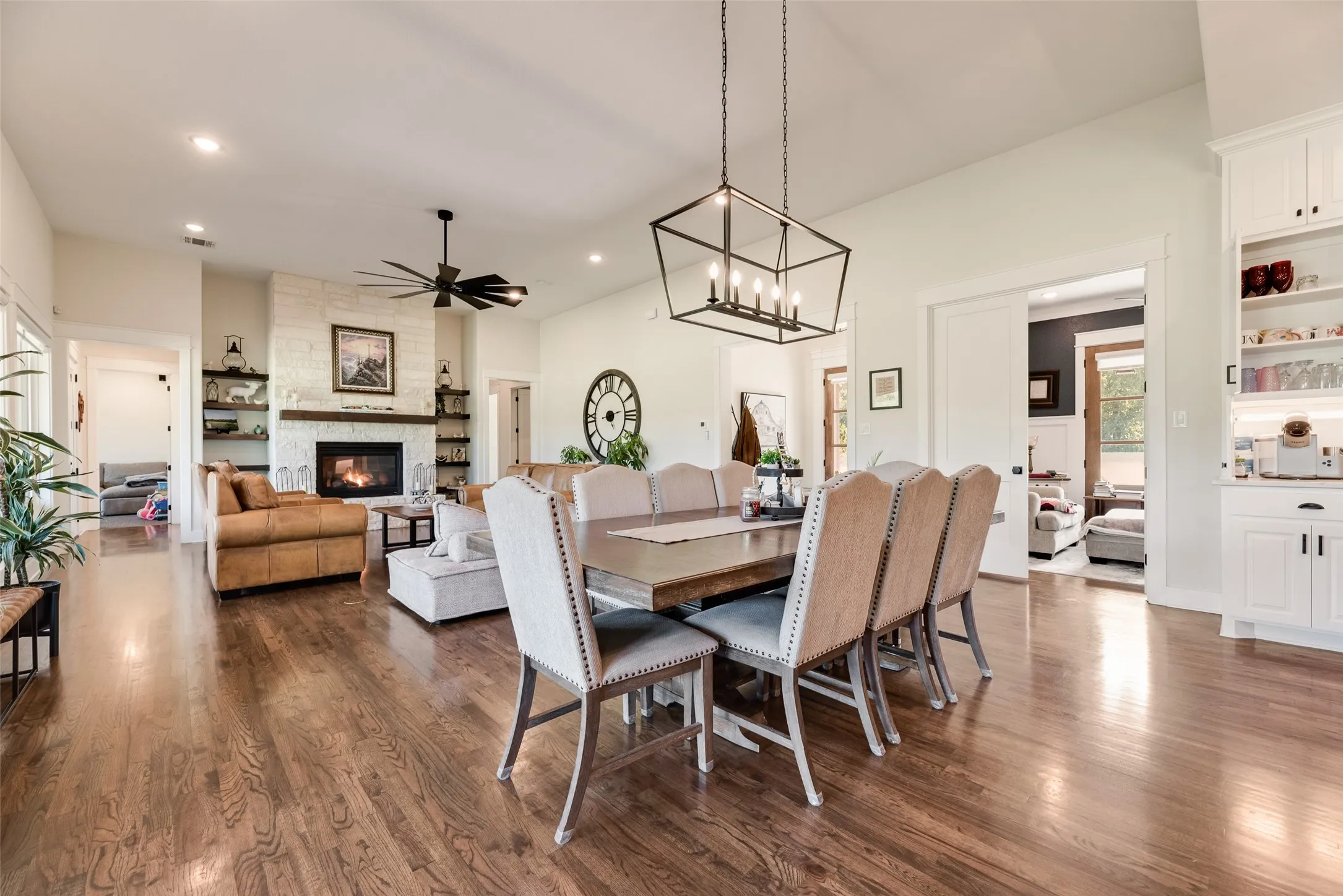 Open-concept living space featuring wood-finish flooring, a white brick fireplace with a wood mantel, vaulted ceilings, and recessed lighting