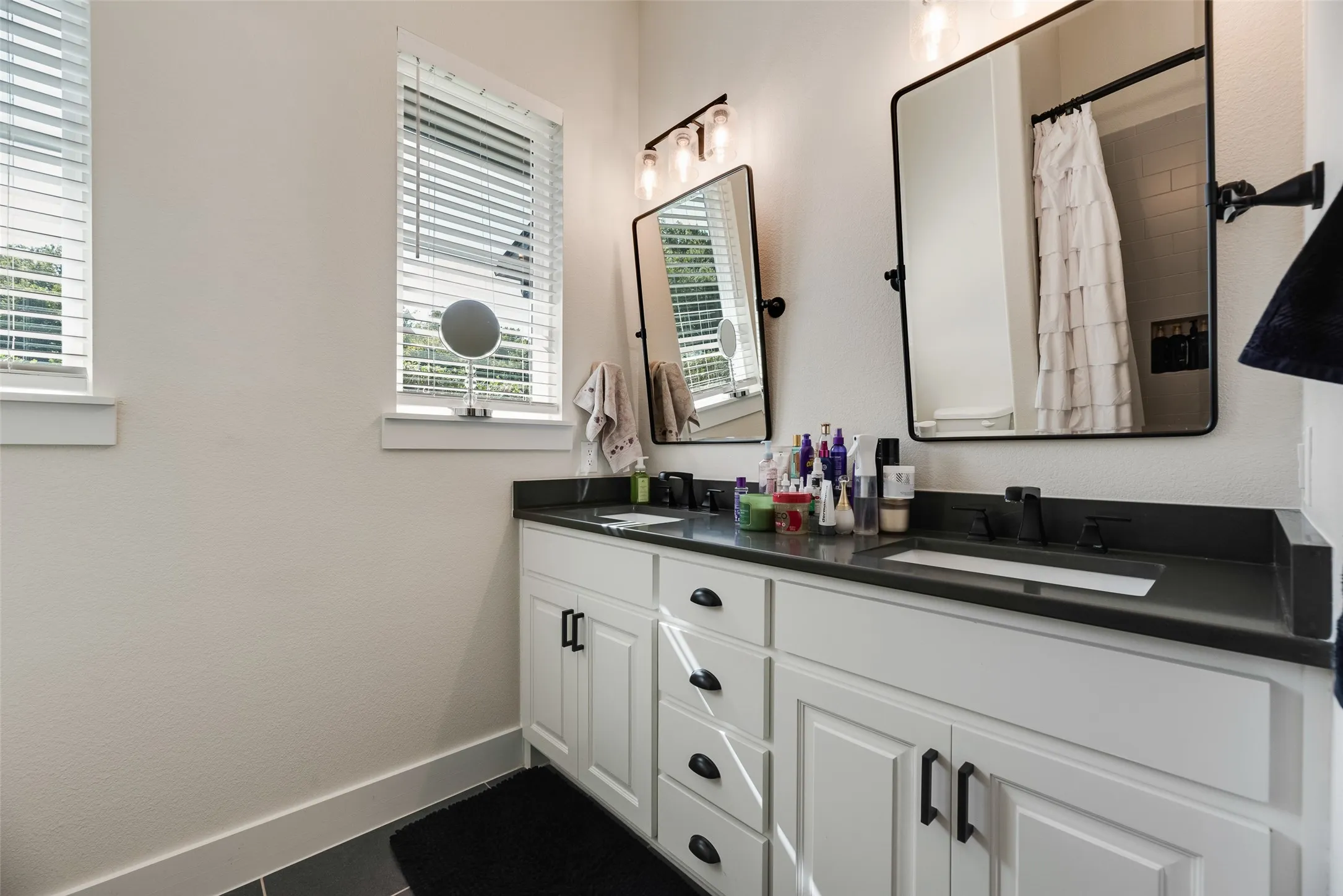 Dual vanity featuring white shaker-style cabinetry with black hardware, dark countertops, and integrated rectangular sinks