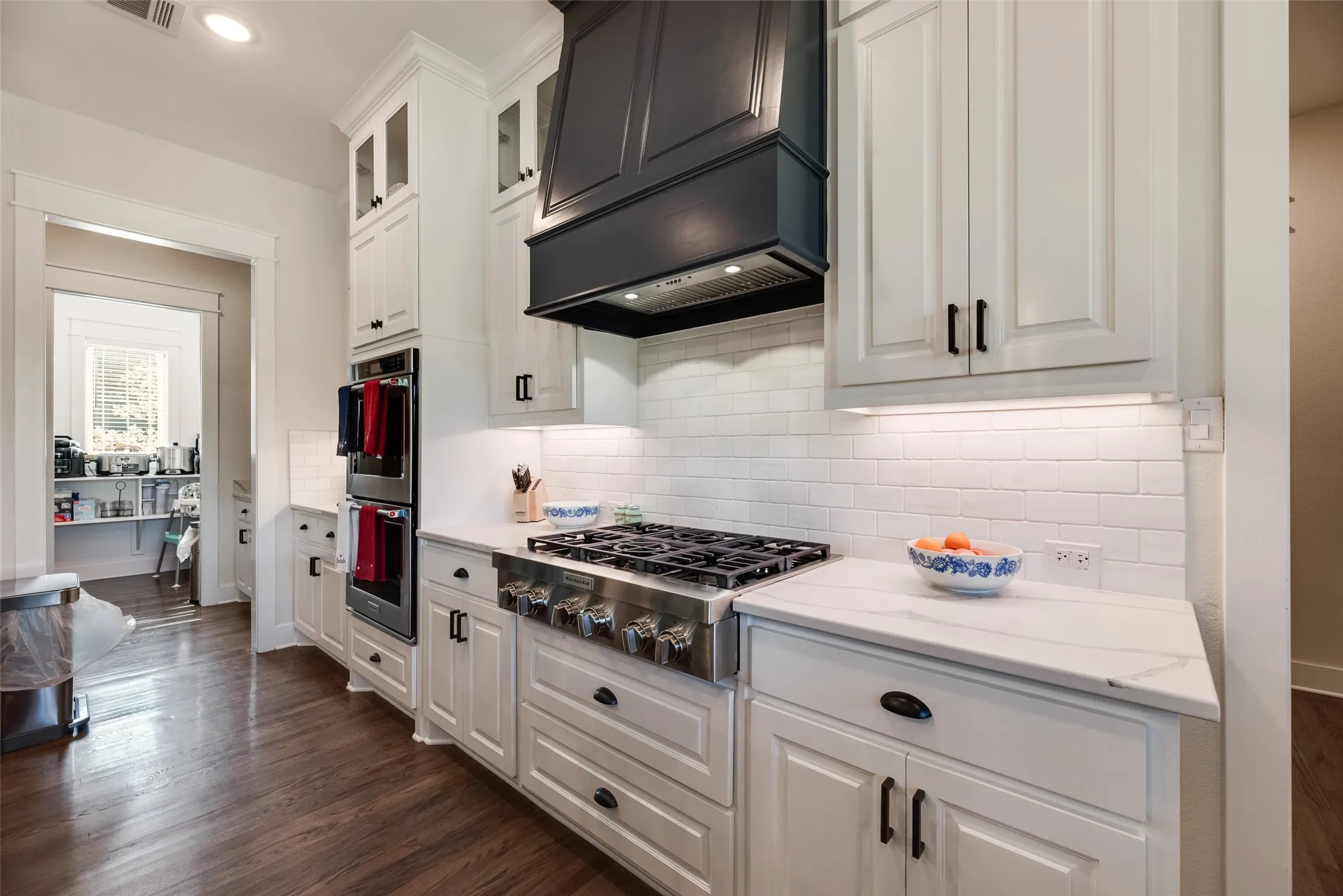 Gourmet kitchen featuring a professional-grade gas range, built-in double ovens, and a dark-finish range hood