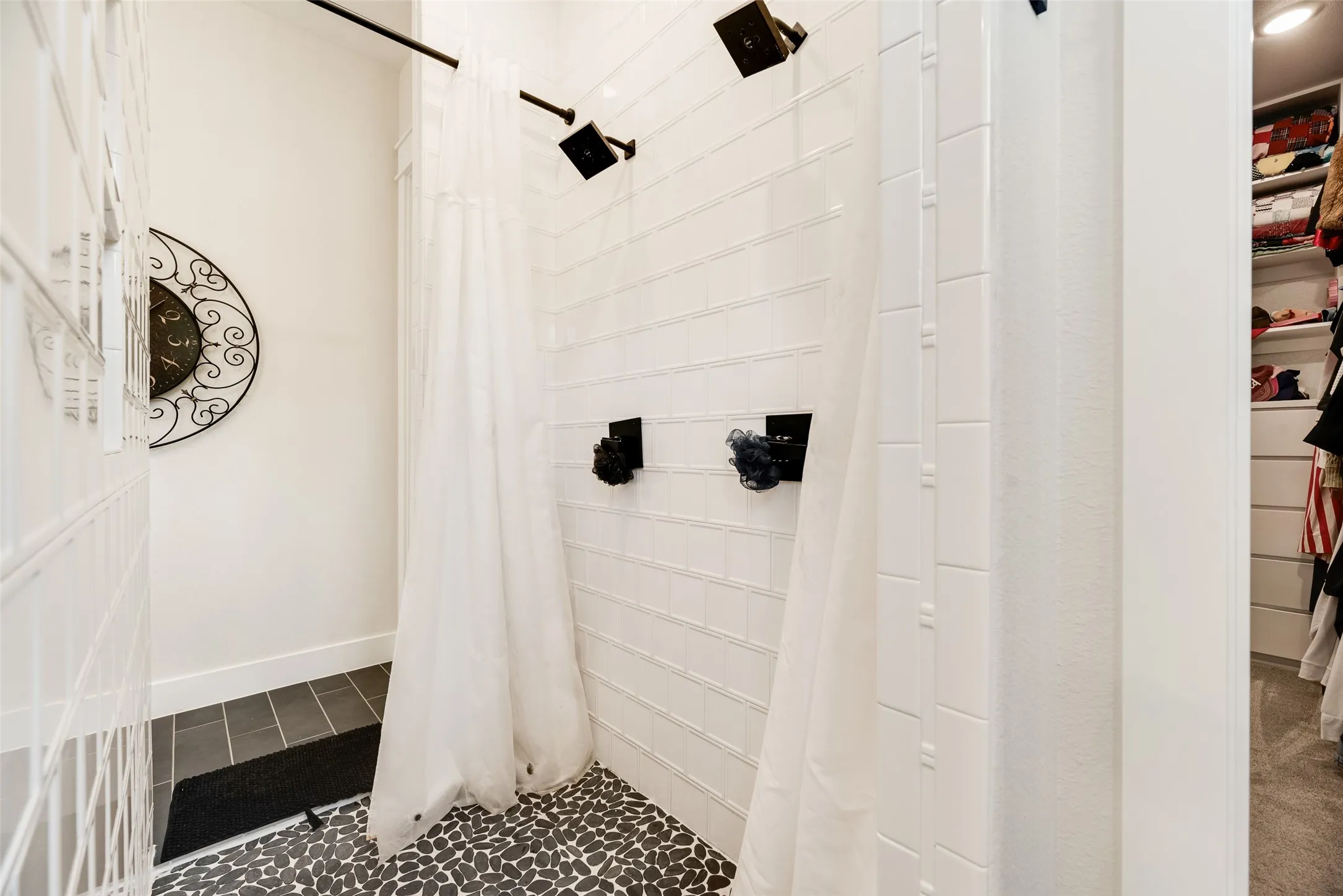 Spacious shower area featuring dual showerheads and matte black hardware, white subway tile walls, and pebble-finish flooring