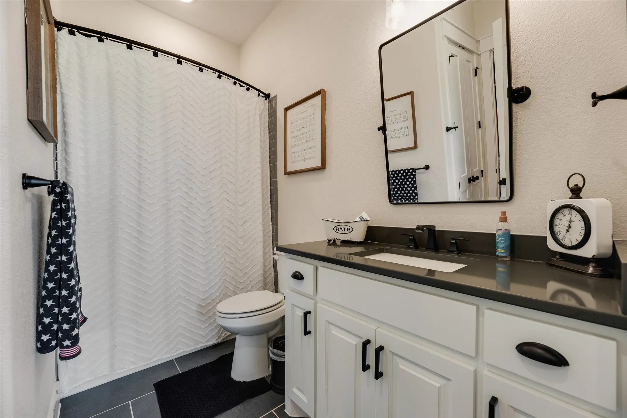 Bathroom featuring a white vanity with dark countertop, undermount sink, and black​​‌​​​​‌​​‌‌​‌‌​​​‌‌​‌​‌​‌​​​‌​​ fixtures
