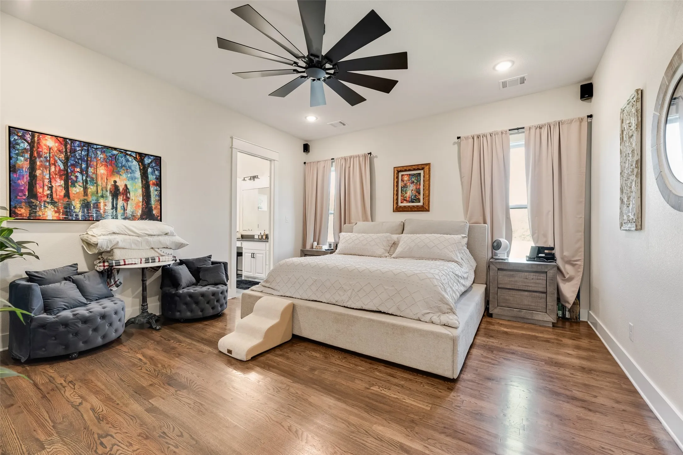 Spacious bedroom featuring rich wood-finish flooring, a contemporary ceiling fan, recessed lighting, and ample natural light from multiple windows