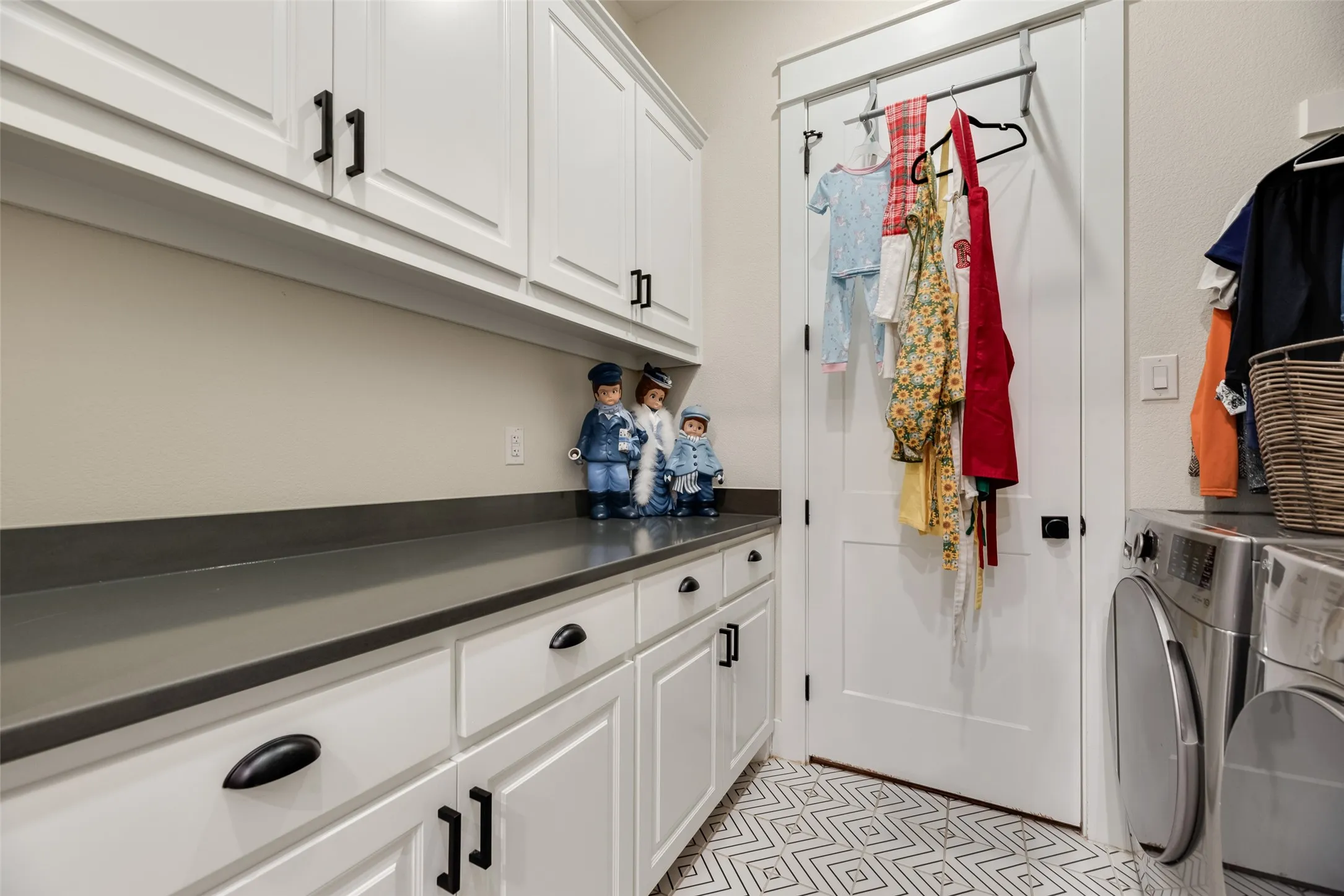 Laundry area featuring white shaker-style cabinetry, dark countertops, and patterned floor tiling